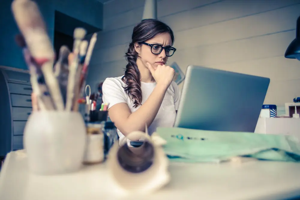 A woman in glasses thinking at her laptop